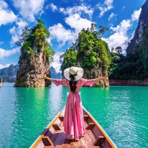 Beautiful girl standing on the boat and looking to mountains in Ratchaprapha Dam at Khao Sok National Park, Surat Thani Province, Thailand.